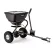 Black tow-behind broadcast spreader with covered hopper, two pneumatic wheels, handle, and hitch bar