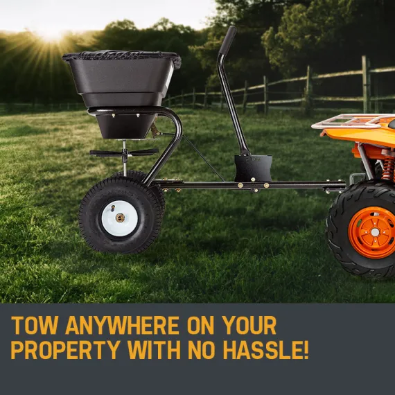 Black spreader attached to an orange utility vehicle on a grassy field
