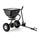 Black tow-behind broadcast spreader with covered hopper, two pneumatic wheels, handle, and hitch bar